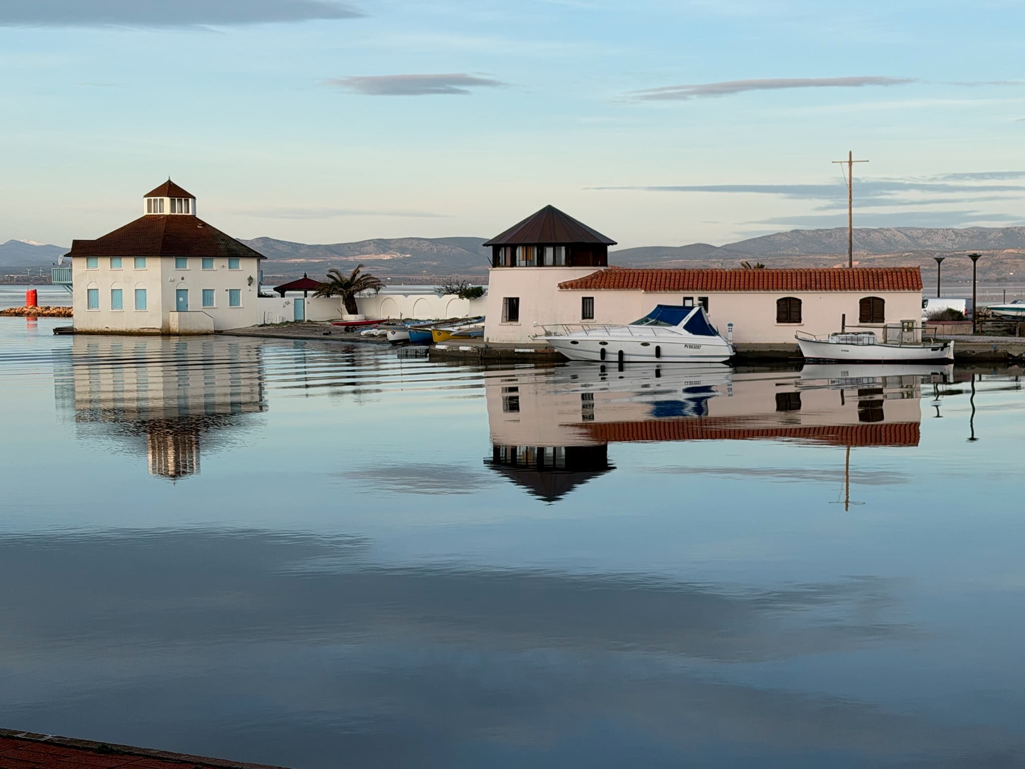 Les deux bâtiments du port de Cap Coudalère au Barcarès, reflétés dans l'eau calme de la lagune, les Corbières à l'horizon